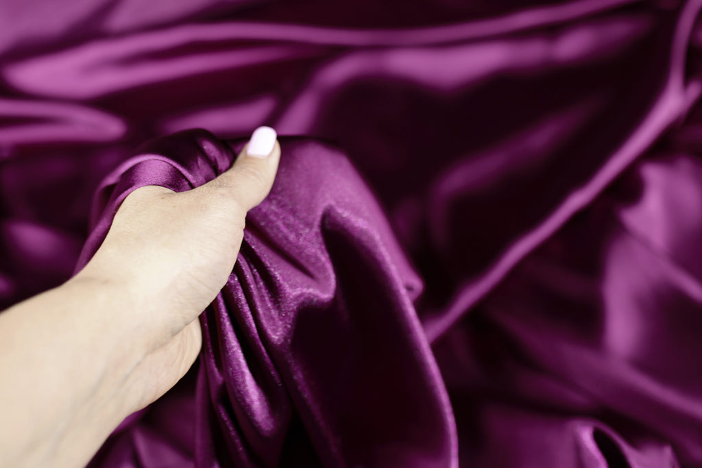 A hand is holding a piece of purple satin fabric, examining it closely.