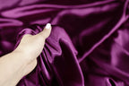 A hand is holding a piece of purple satin fabric, examining it closely.