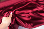 A hand is holding a piece of red satin fabric, with the fabric's folds and creases visible.