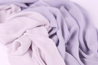 The image is a close-up of a soft, flowing fabric in shades of purple and pink, with a slightly crumpled texture.