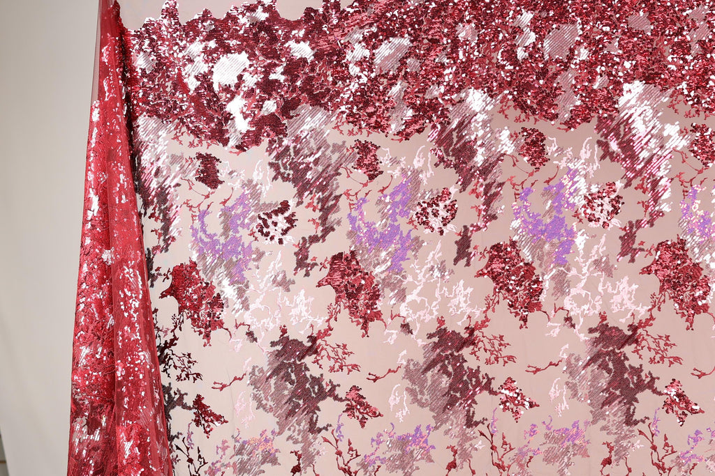 a fabric with a red and pink floral pattern, with the red fabric partially covering the pink fabric. The fabric appears to be made of sequin material, creating a visually striking and vibrant design.