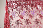 a fabric with a red and pink floral pattern, with the red fabric partially covering the pink fabric. The fabric appears to be made of sequin material, creating a visually striking and vibrant design.