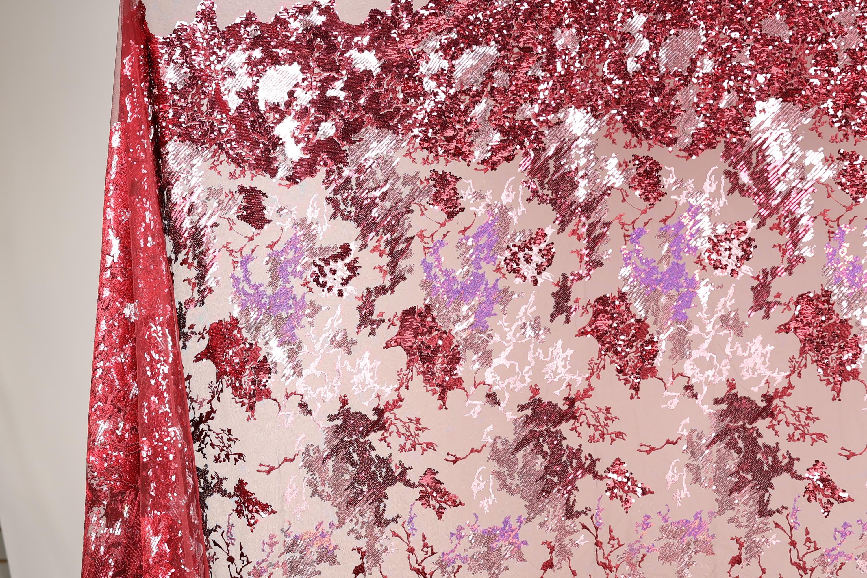 a fabric with a red and pink floral pattern, with the red fabric partially covering the pink fabric. The fabric appears to be made of sequin material, creating a visually striking and vibrant design.