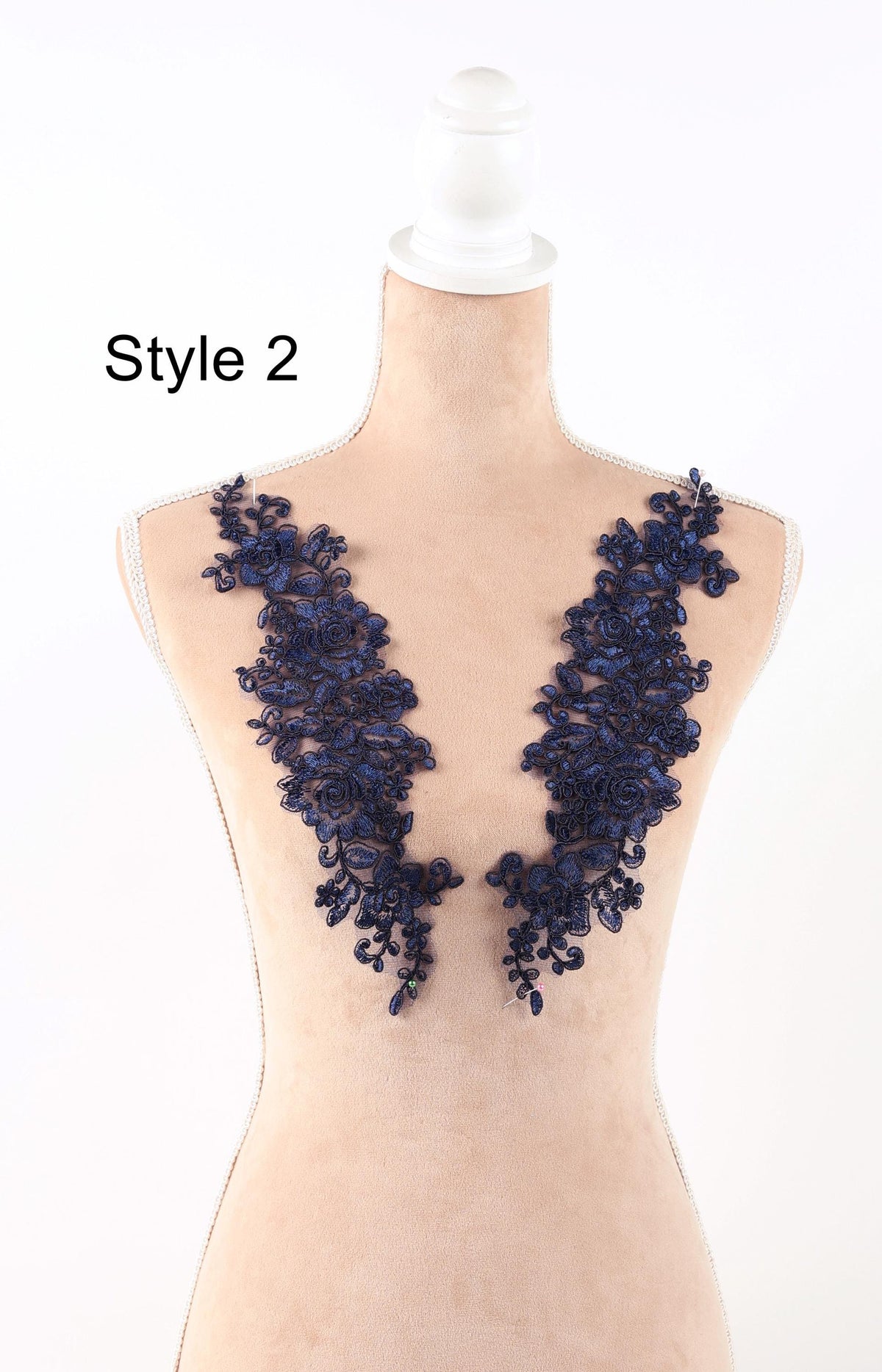 A mannequin wearing a beige dress with blue floral lace appliques on the bust area.