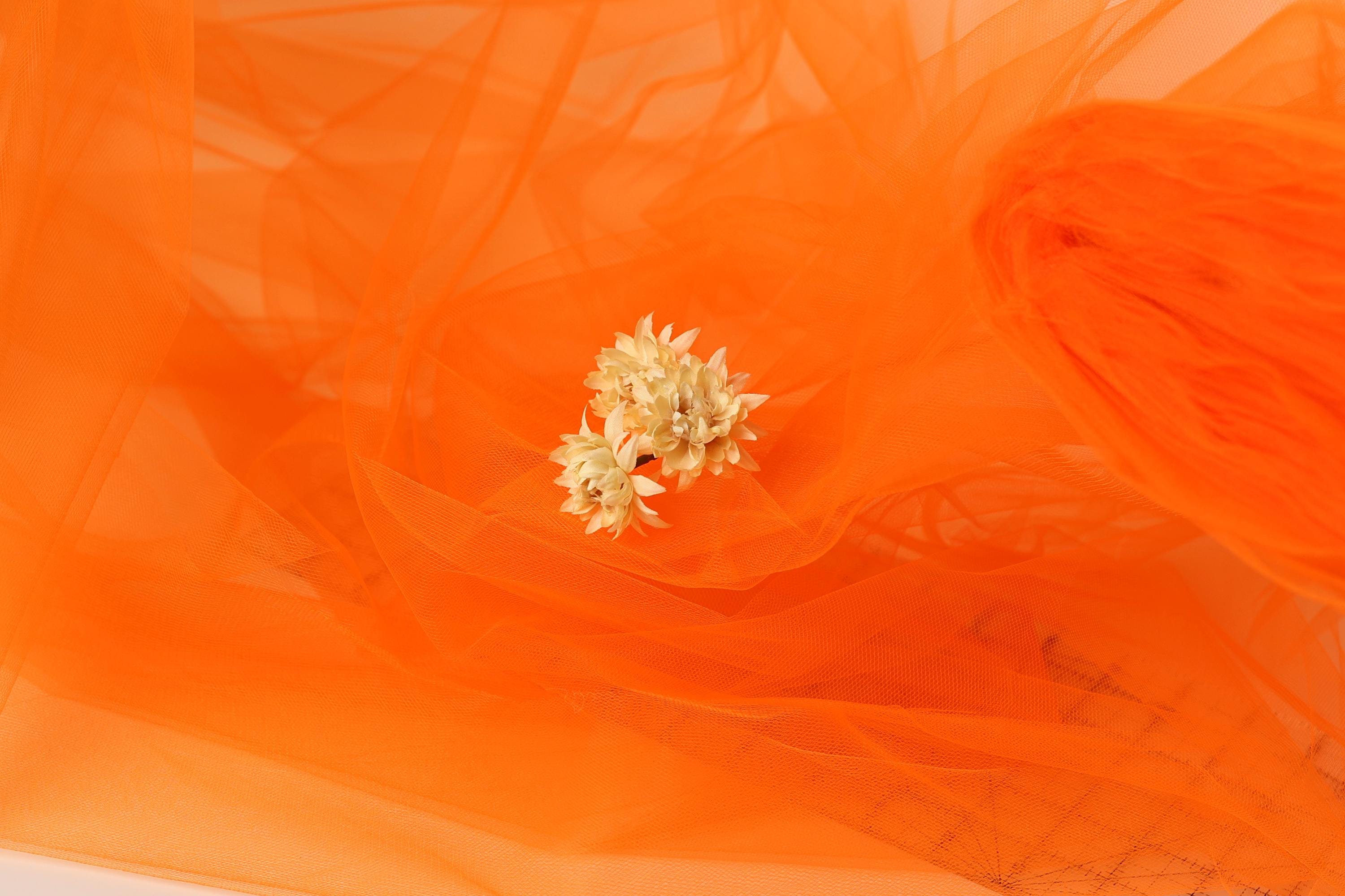 a close-up view of a small white flower resting on a vibrant orange fabric.