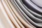 A close-up view of a fabric with a gradient of colors, transitioning from light to dark shades of gray and beige.