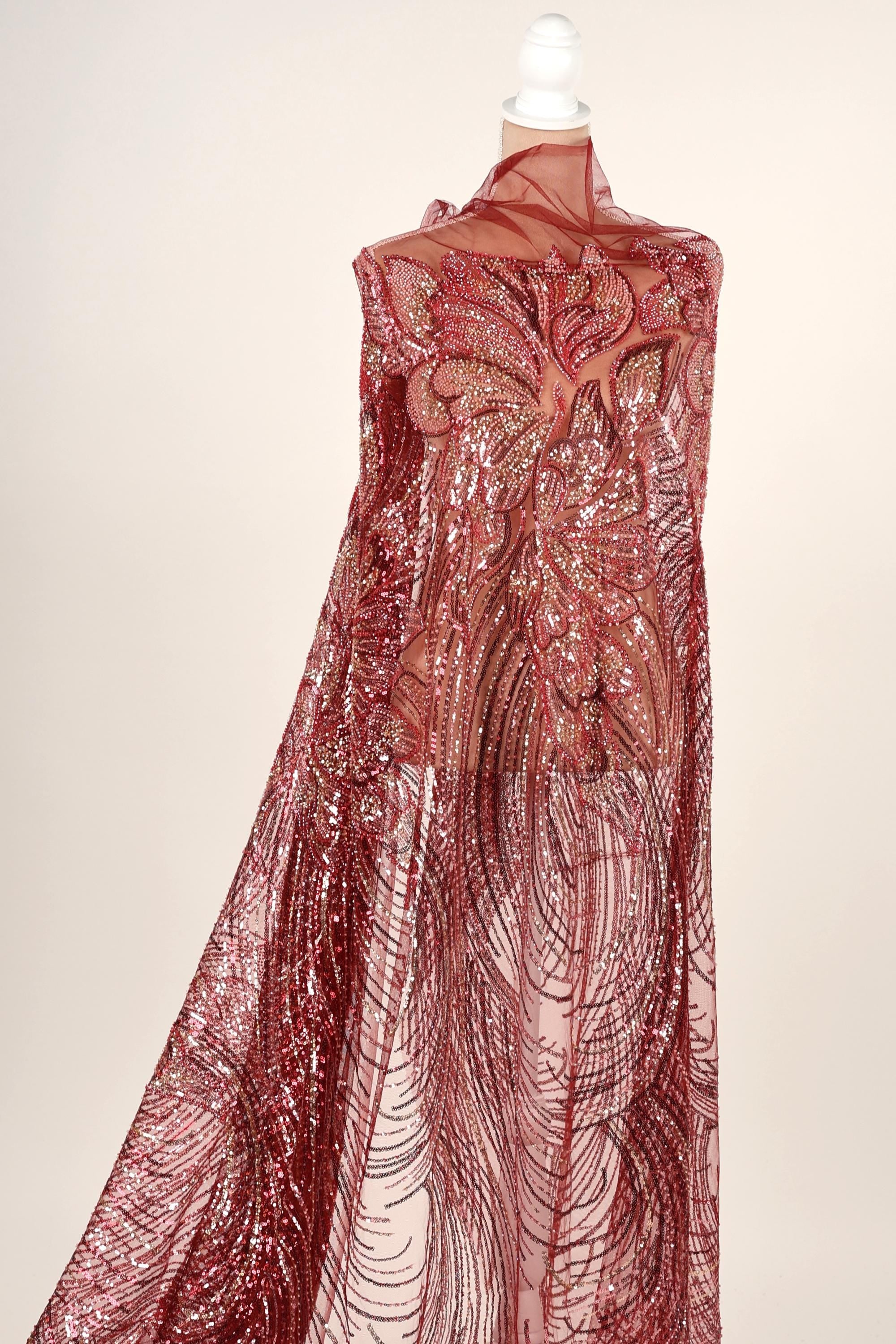 A mannequin wearing a long, flowing red sequin dress with a floral pattern.