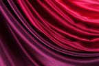 a close-up view of a fabric with a gradient of colors, transitioning from a deep red to a lighter purple. The fabric appears to be made of satin or a similar smooth, shiny material, and it has a flowing, draped appearance.