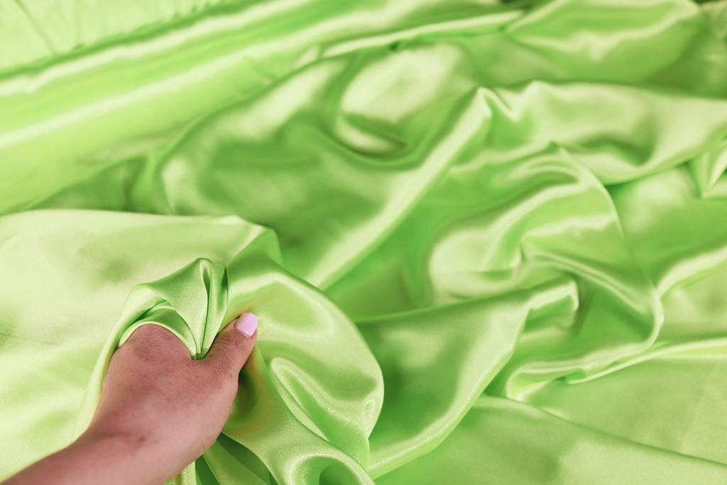 A hand is holding a piece of green satin fabric, which appears to be soft and smooth.