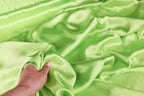 A hand is holding a piece of green satin fabric, which appears to be soft and smooth.