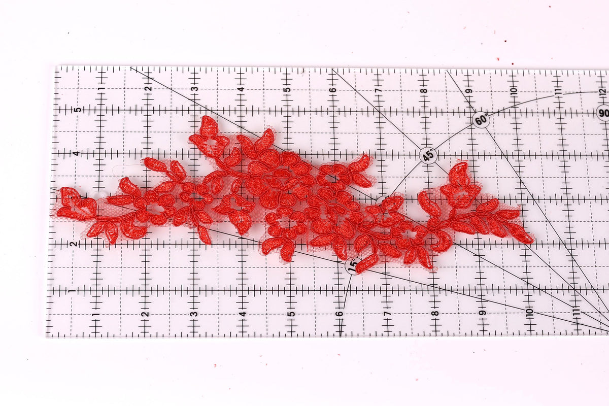 a clear ruler with red floral embroidery pieces placed on it.