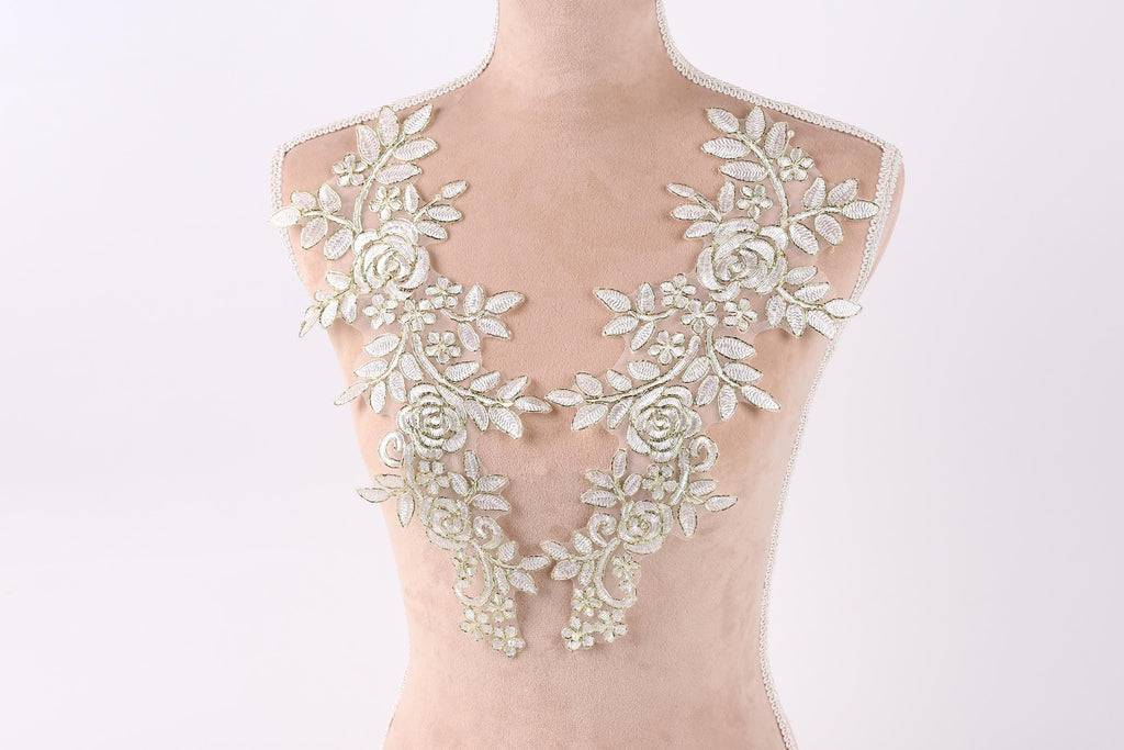 A mannequin wearing a white lace dress with intricate floral embroidery on the shoulders and neck.