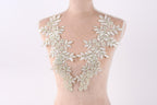 A mannequin wearing a white lace dress with intricate floral embroidery on the shoulders and neck.