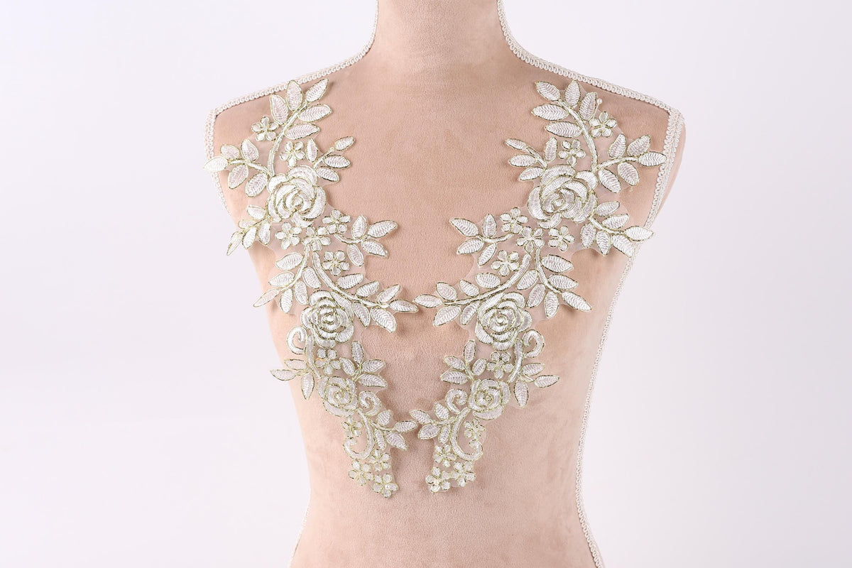 A mannequin wearing a white lace dress with intricate floral embroidery on the shoulders and neck.