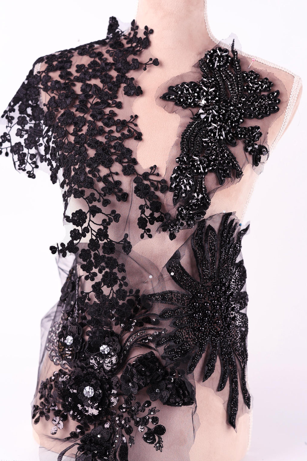 A mannequin wearing a black dress with intricate lace and floral embroidery details.