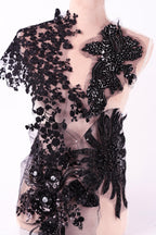 A mannequin wearing a black dress with intricate lace and floral embroidery details.