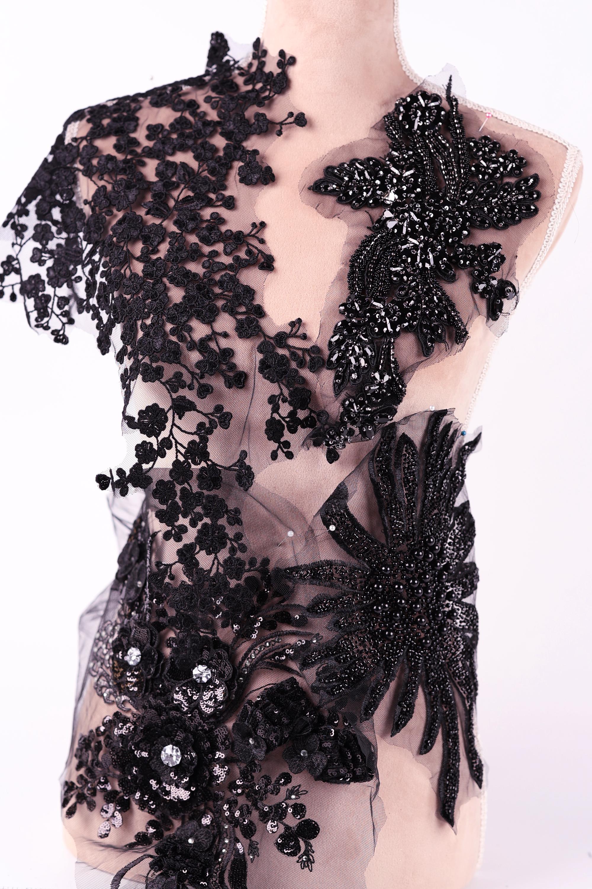 A mannequin wearing a black dress with intricate lace and floral embroidery details.