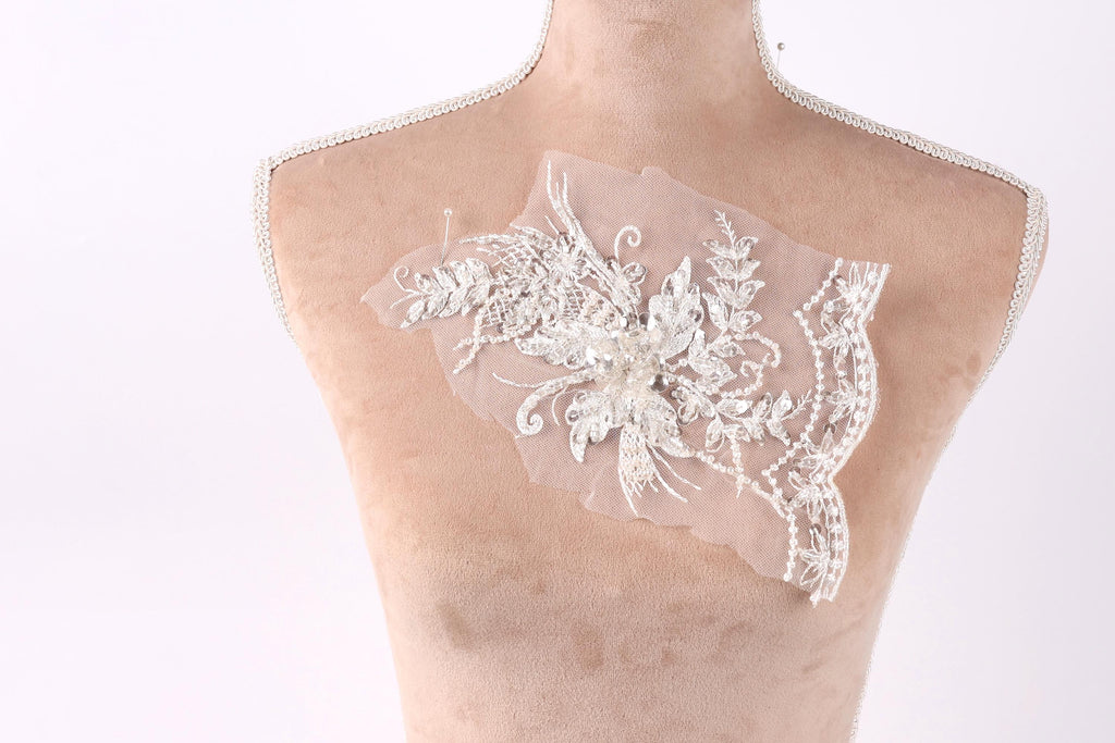 A mannequin torso with a delicate, intricate piece of white lace embroidery on it.