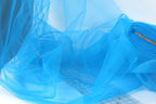 a close-up view of a blue, sheer fabric or chiffon material, with a grid pattern visible underneath. The fabric appears to be folded or crumpled, creating a textured and flowing appearance.