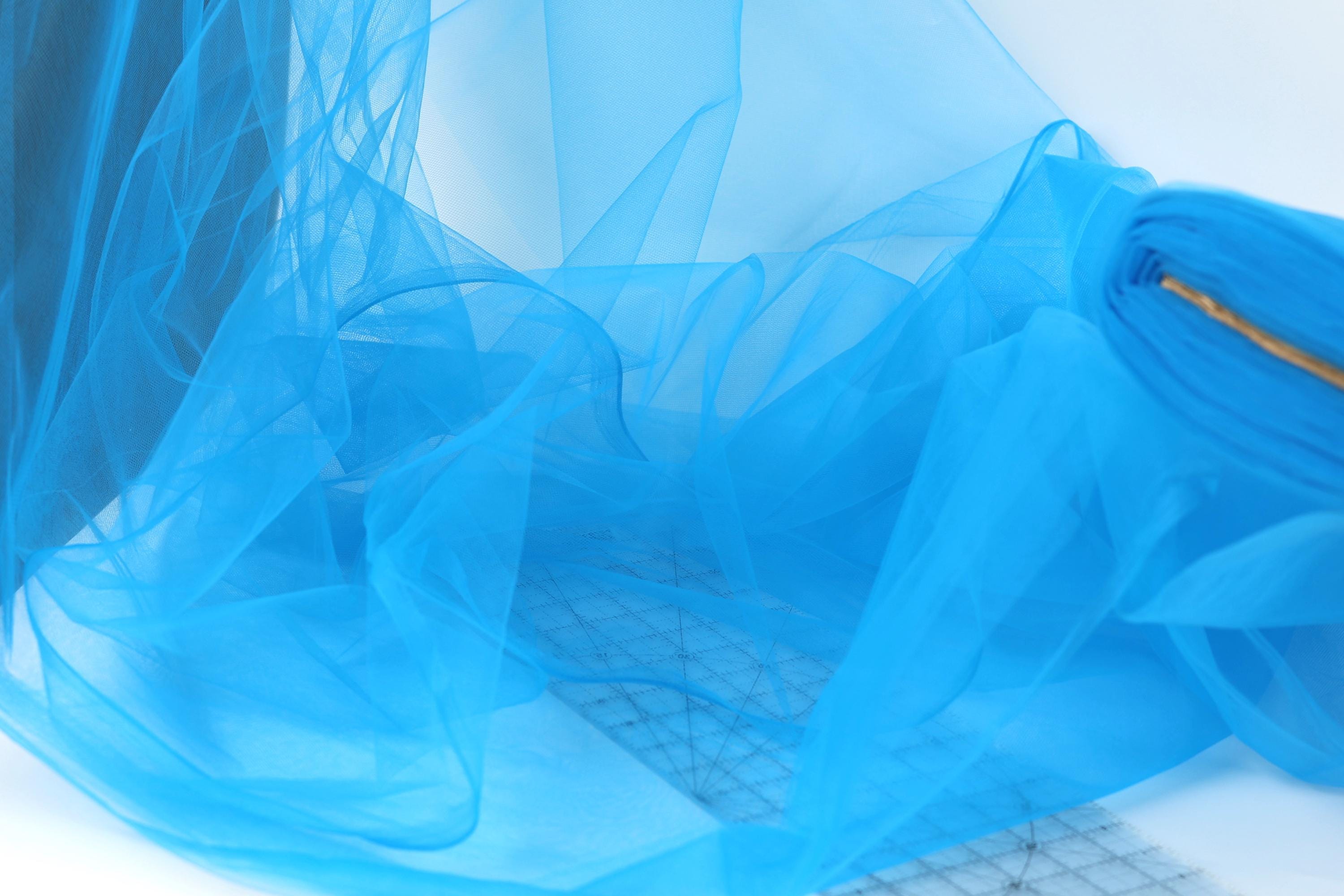 a close-up view of a blue, sheer fabric or chiffon material, with a grid pattern visible underneath. The fabric appears to be folded or crumpled, creating a textured and flowing appearance.