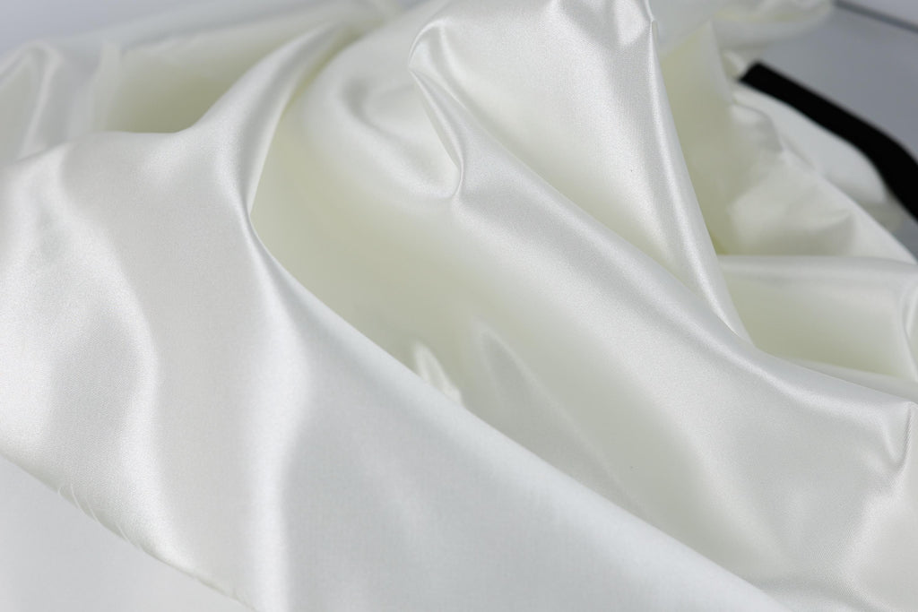 The image is a close-up of a white fabric, possibly silk or satin, with a smooth and shiny texture.