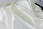 The image is a close-up of a white fabric, possibly silk or satin, with a smooth and shiny texture.