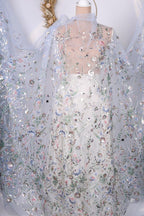 a white dress with a sheer, floral-patterned cape draped over it. The dress appears to be made of sheer fabric, giving it a delicate and elegant appearance. The cape is adorned with a floral design, adding a touch of sophistication to the overall look. The dress and cape are displayed against a white background, which further accentuates their colors and patterns.