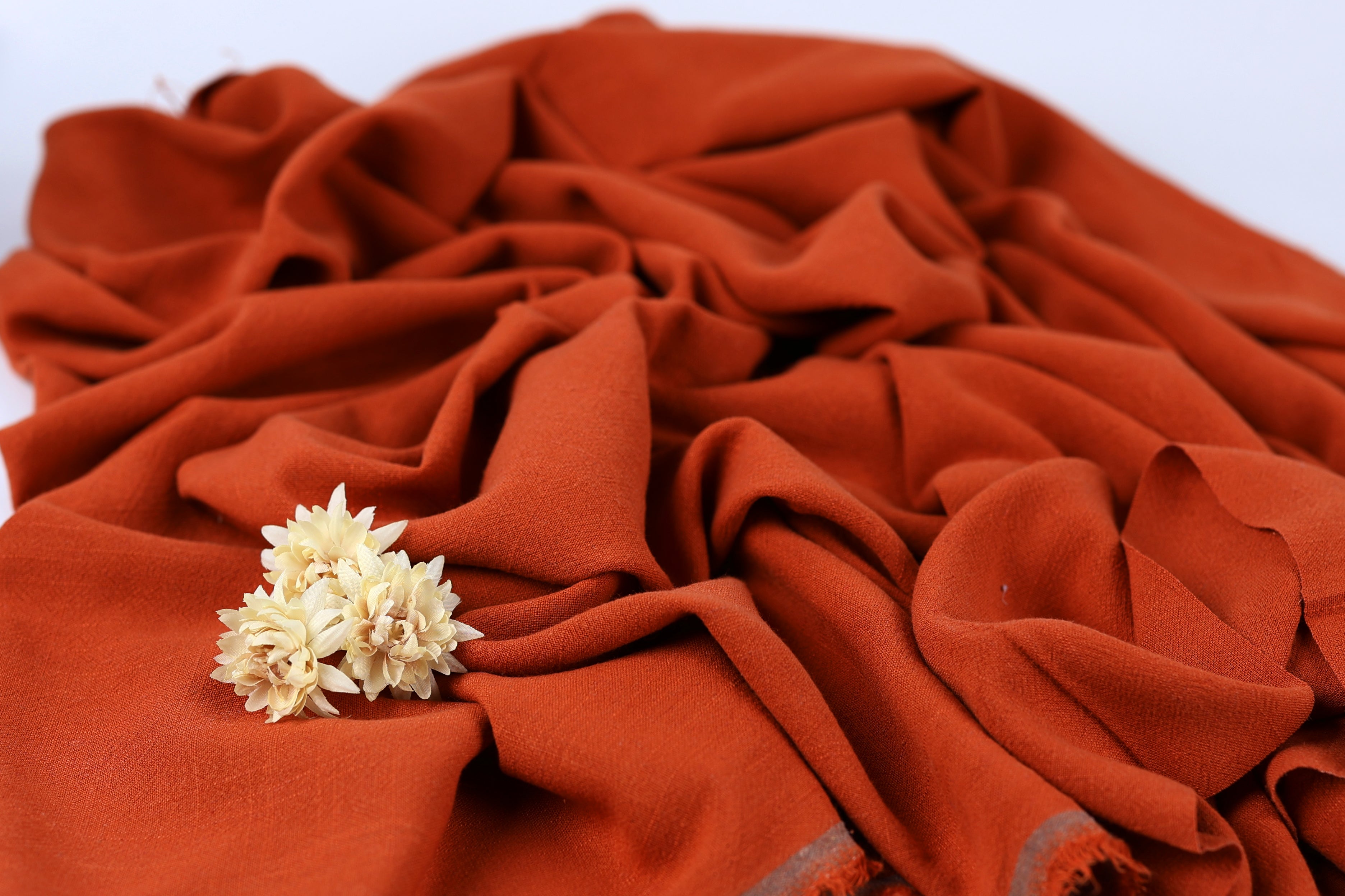 a close-up view of a crumpled orange fabric with a single white flower resting on it.