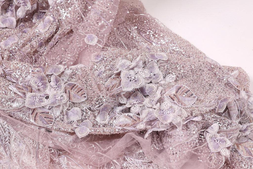 The image is a close-up of a delicate, intricately designed fabric with a floral pattern. The fabric appears to be made of lace or a similar material, with a soft, pastel color palette. The floral pattern consists of small, delicate flowers and leaves, creating a visually appealing and intricate design.