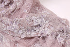 The image is a close-up of a delicate, intricately designed fabric with a floral pattern. The fabric appears to be made of lace or a similar material, with a soft, pastel color palette. The floral pattern consists of small, delicate flowers and leaves, creating a visually appealing and intricate design.