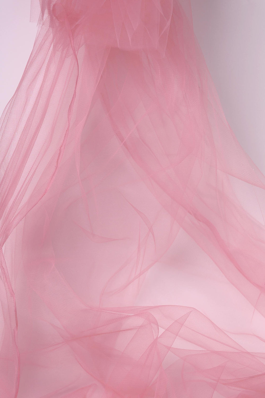 The image is a close-up of a soft, flowing pink fabric, possibly tulle, with a delicate and ethereal texture.