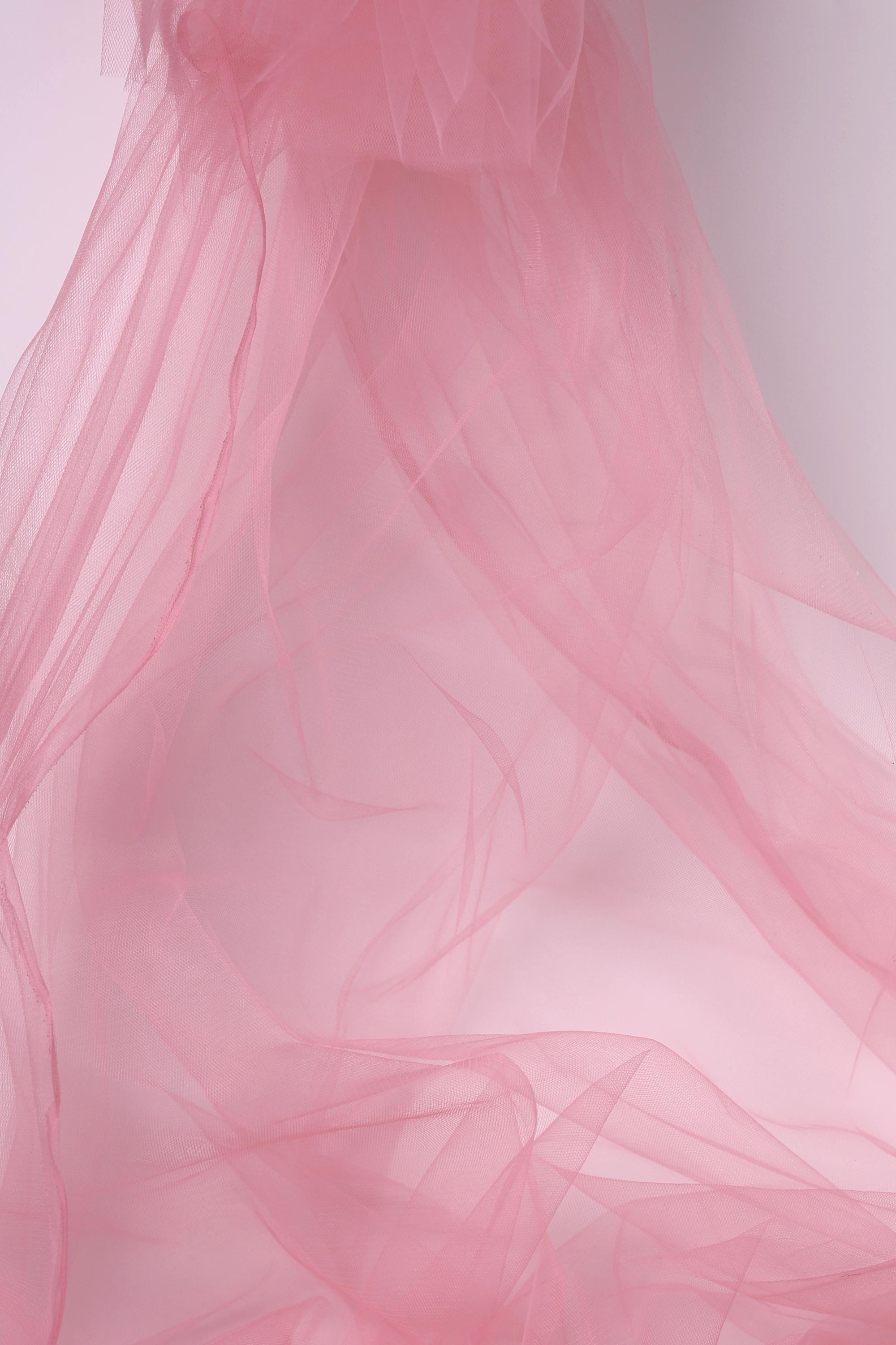 The image is a close-up of a soft, flowing pink fabric, possibly tulle, with a delicate and ethereal texture.