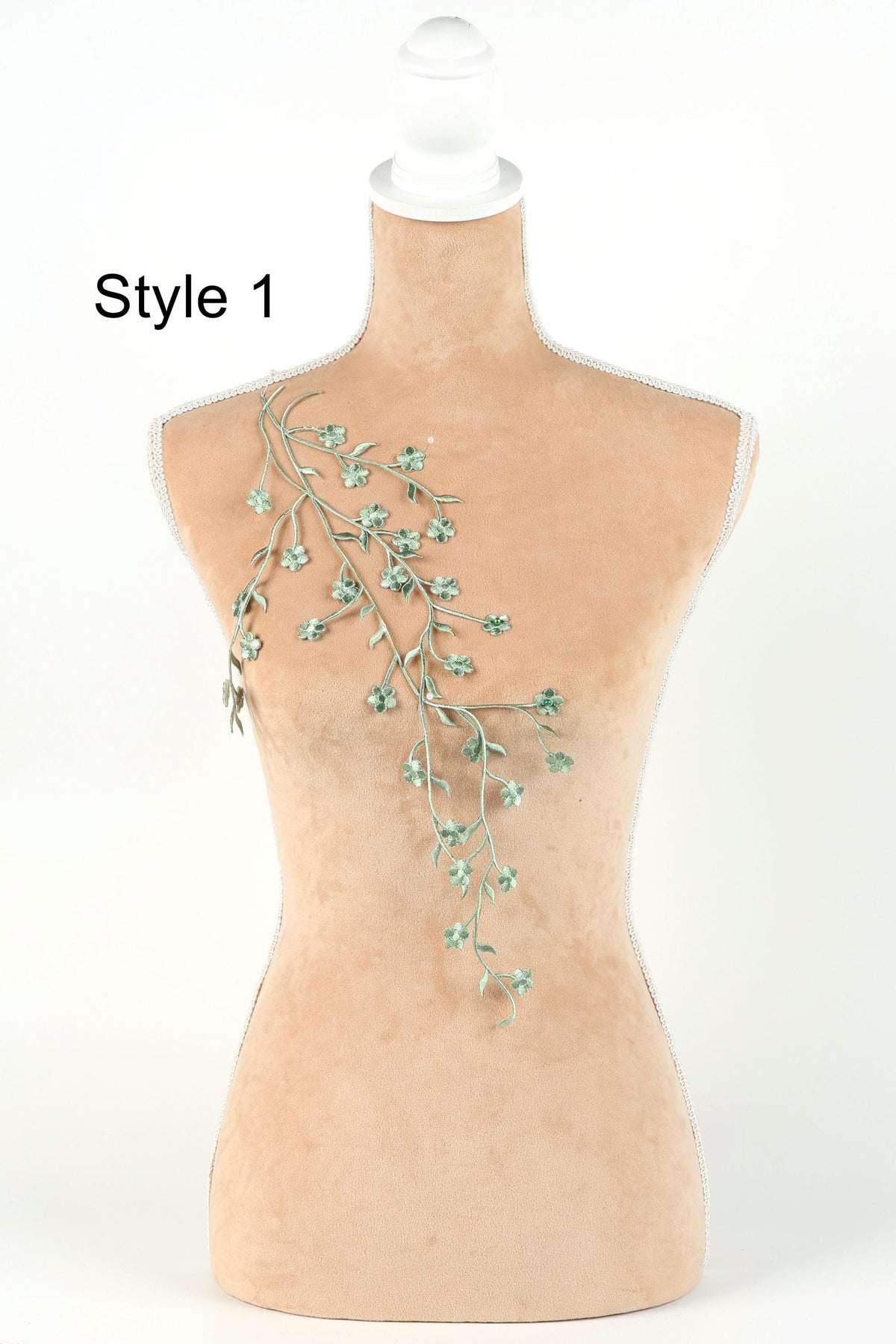 A mannequin with a floral embroidered on its bust, featuring a branch with green leaves and flowers.