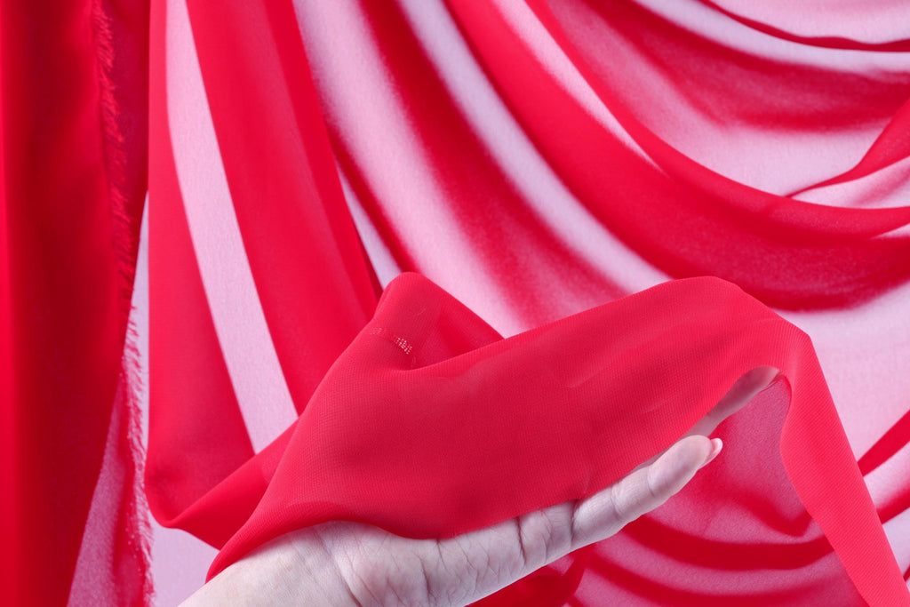 A hand is holding a red fabric against a background of red and white striped fabric.