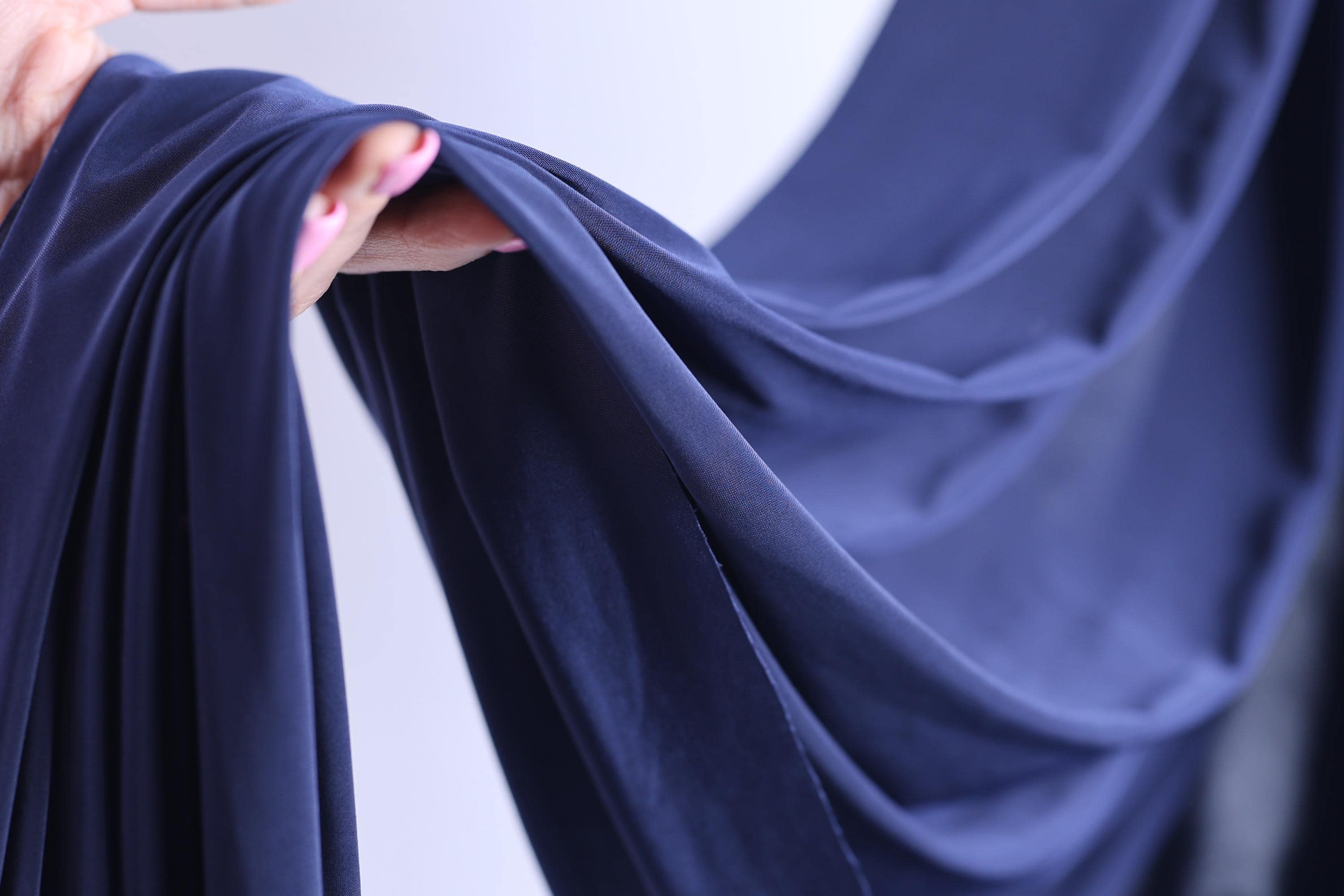 A hand is holding a piece of blue fabric, which appears to be a close-up view of the fabric.