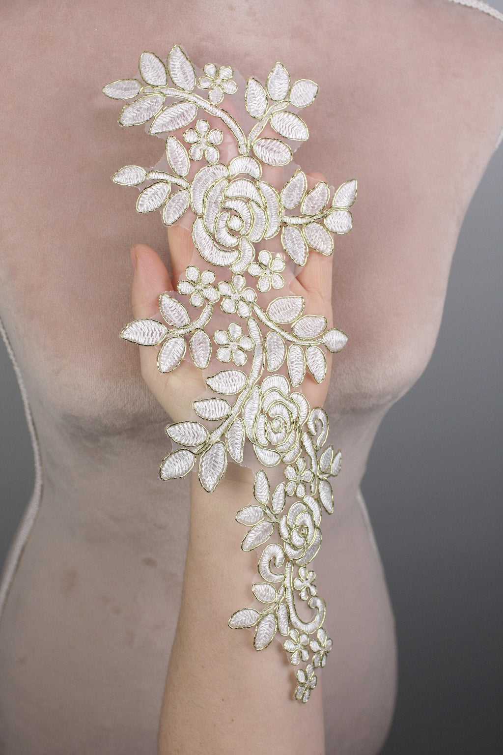 A hand holding a delicate, intricately designed piece of lace or embroidery with a floral pattern.