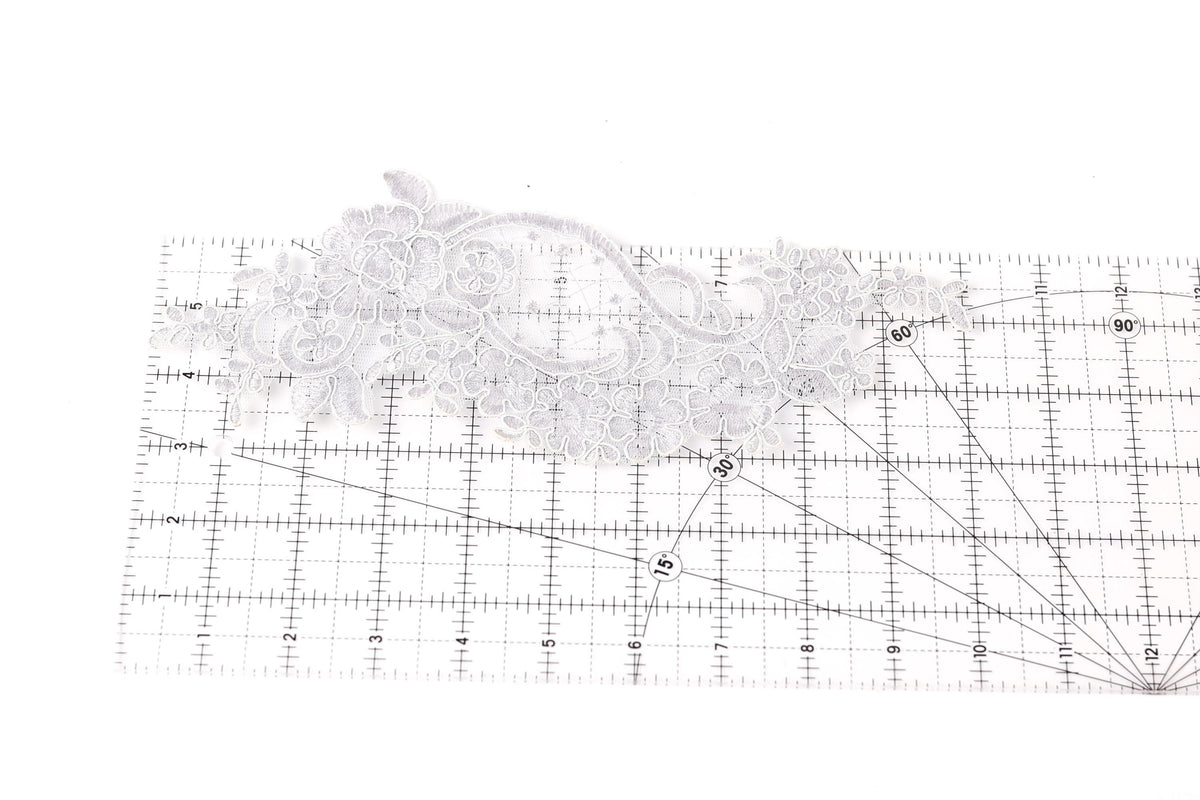 a close-up view of a piece of white lace with intricate floral patterns, placed on a ruler for scale.