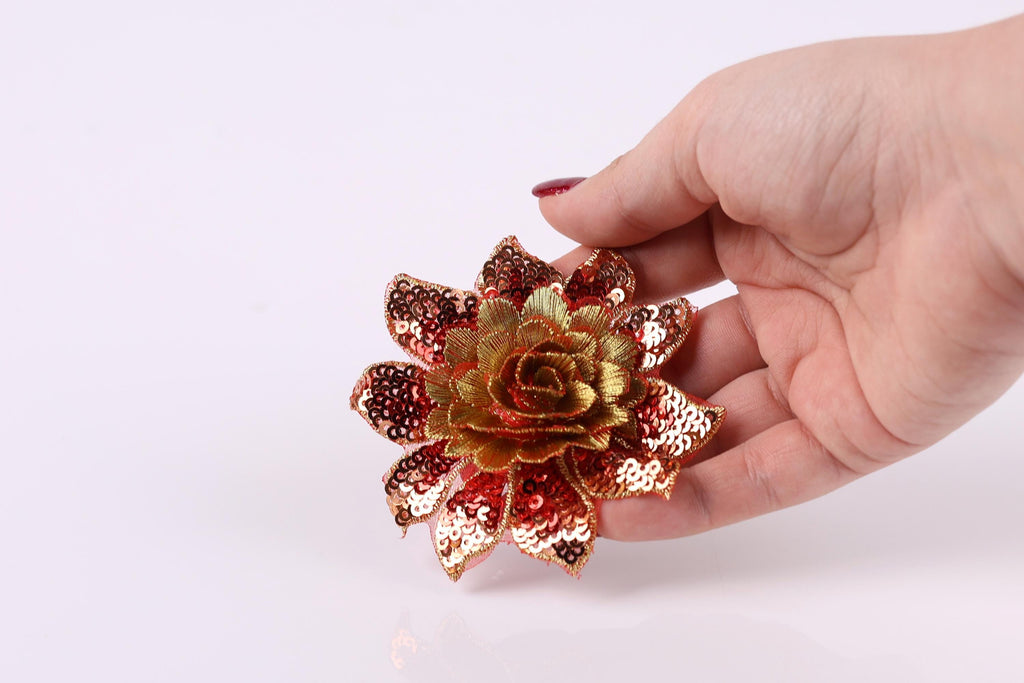 A hand holding a decorative flower with sequin details against a white background.