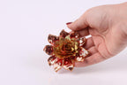 A hand holding a decorative flower with sequin details against a white background.