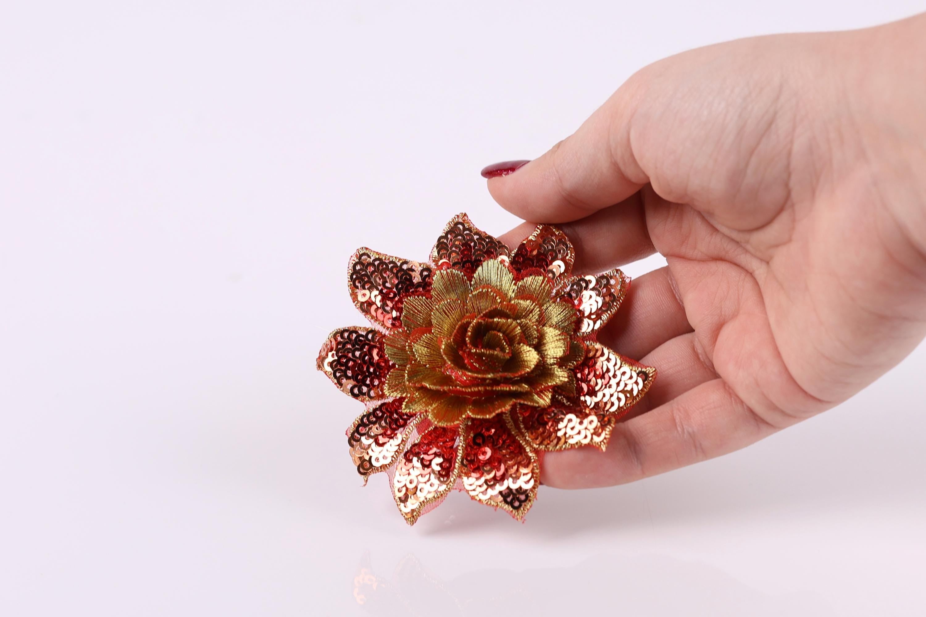 A hand holding a decorative flower with sequin details against a white background.