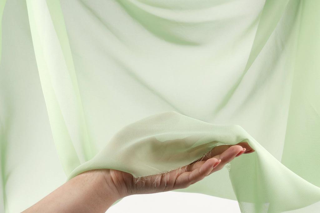 A hand holding a piece of green fabric against a blurred green background.