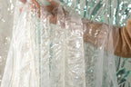 A hand is holding a white fabric with sequin details, partially covering a person's arm.