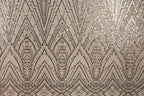 a close-up view of a fabric with a repeating pattern of diamond-shaped sequins in shades of brown and beige. The pattern is intricate and detailed, with the sequins arranged in a zigzag or diagonal pattern across the fabric. The overall appearance of the fabric is visually striking and textured, with the sequins adding a touch of sparkle and elegance to the design.