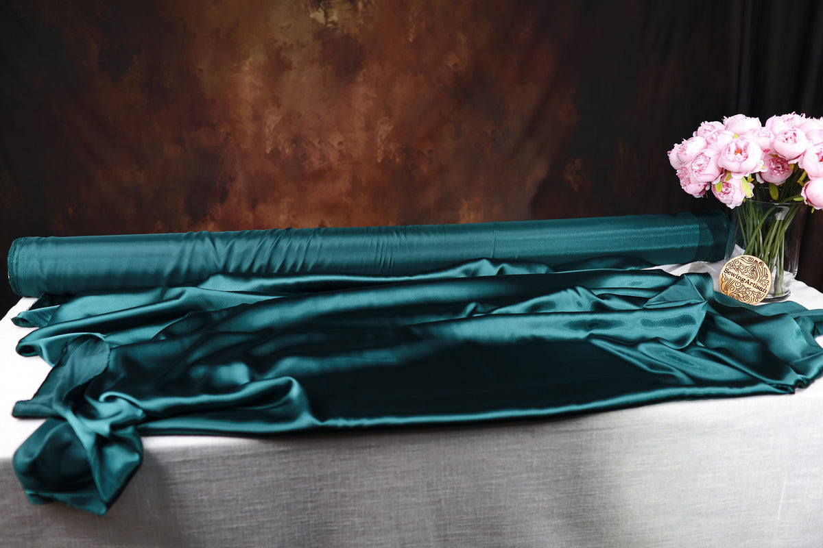 a roll of green satin fabric, a vase of pink flowers, and a dark background.