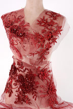 A mannequin wearing a red dress with intricate floral embroidery and sequin details.