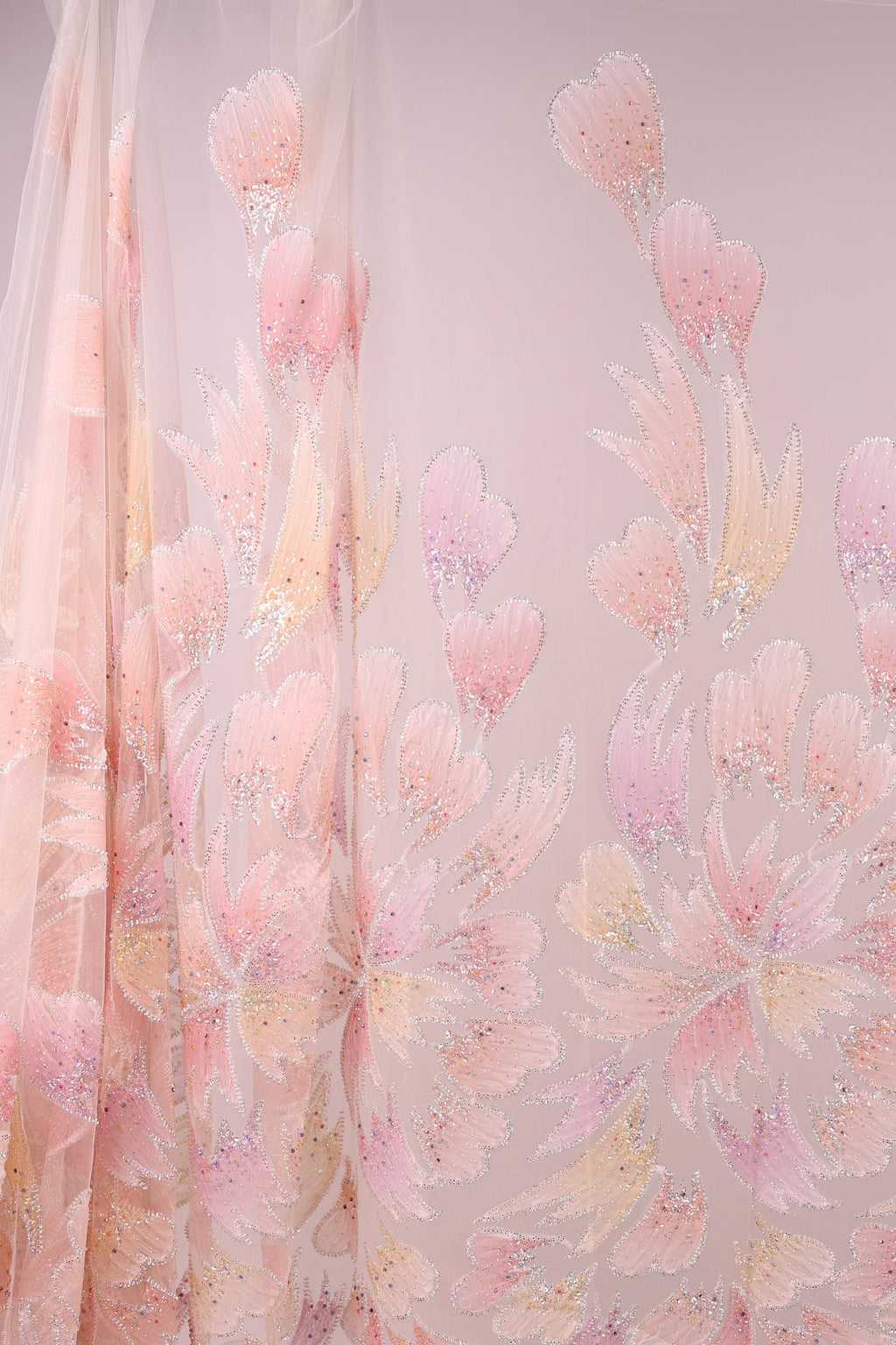 a fabric with a floral pattern in shades of pink and white. The fabric appears to be made of sheer material, giving it a delicate and airy appearance. The pattern consists of various pink and white flowers and leaves, creating a visually appealing and intricate design.