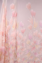 a fabric with a floral pattern in shades of pink and white. The fabric appears to be made of sheer material, giving it a delicate and airy appearance. The pattern consists of various pink and white flowers and leaves, creating a visually appealing and intricate design.