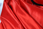 A close-up view of a red satin fabric, with a black collar visible.