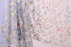 a close-up view of a delicate, floral-patterned fabric, with a blend of pink, green, and white colors. The fabric appears to be made of sheer material, giving it a soft and delicate appearance. The intricate floral designs and patterns on the fabric create a visually appealing and textured surface.