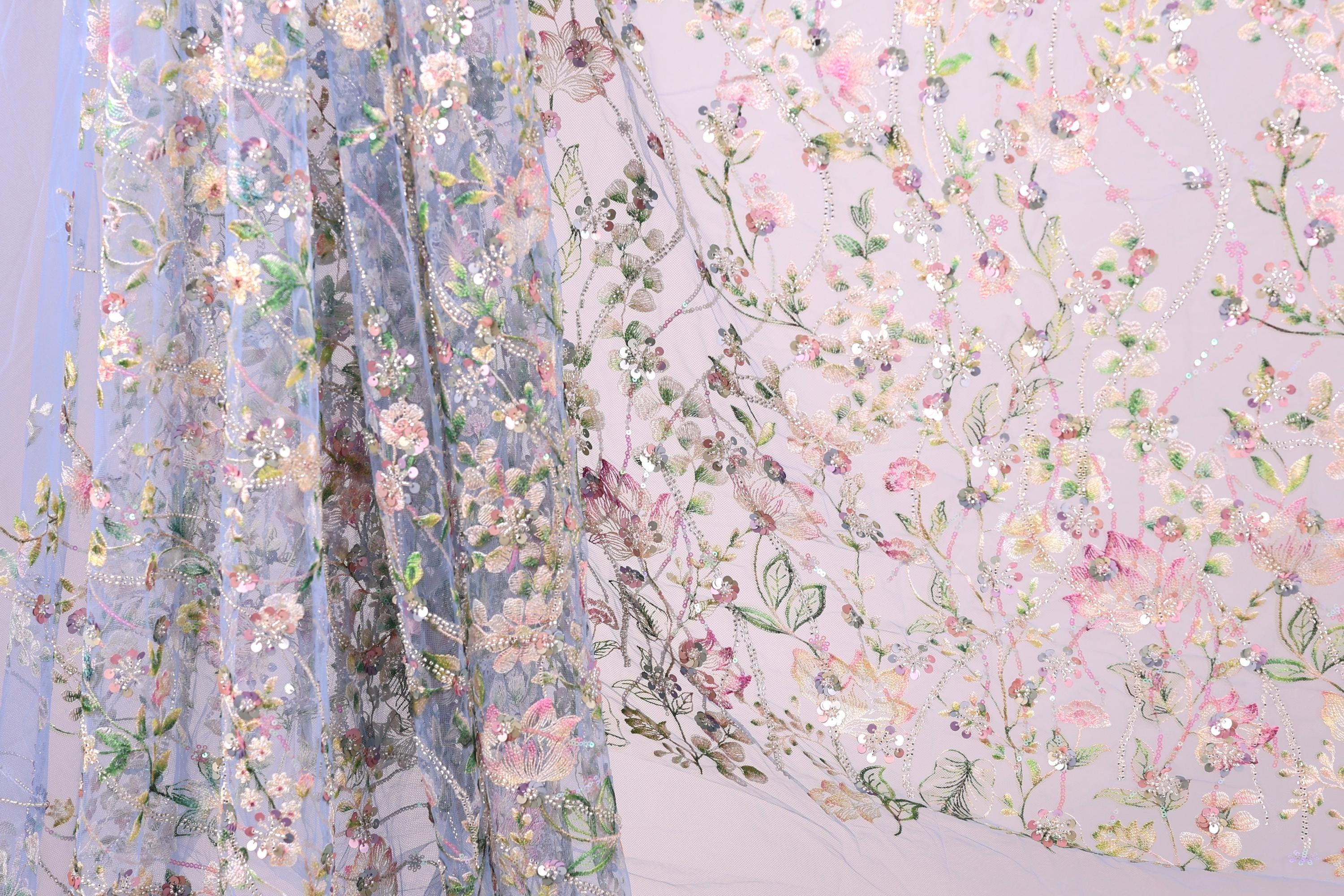 a close-up view of a delicate, floral-patterned fabric, with a blend of pink, green, and white colors. The fabric appears to be made of sheer material, giving it a soft and delicate appearance. The intricate floral designs and patterns on the fabric create a visually appealing and textured surface.